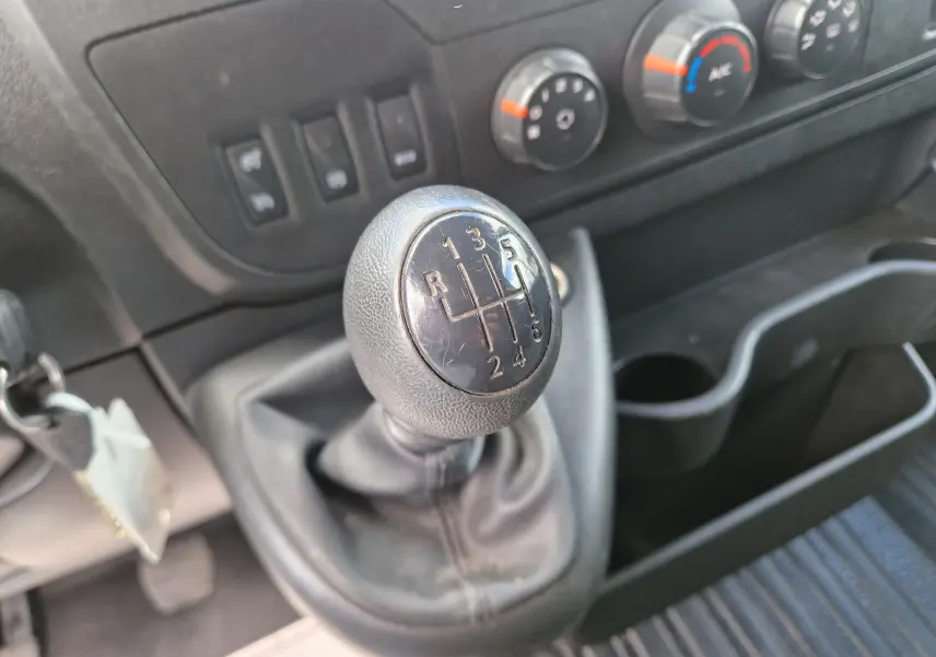 Gros plan sur le levier de vitesses manuel noir du Renault Master blanc, avec commandes de climatisation en arrière-plan.