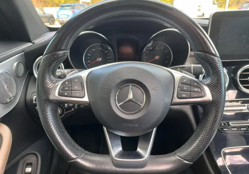 Vue rapprochée du volant cuir noir multifonctions d’une Mercedes Classe C Coupé 2016, tableau de bord et écran central visibles.