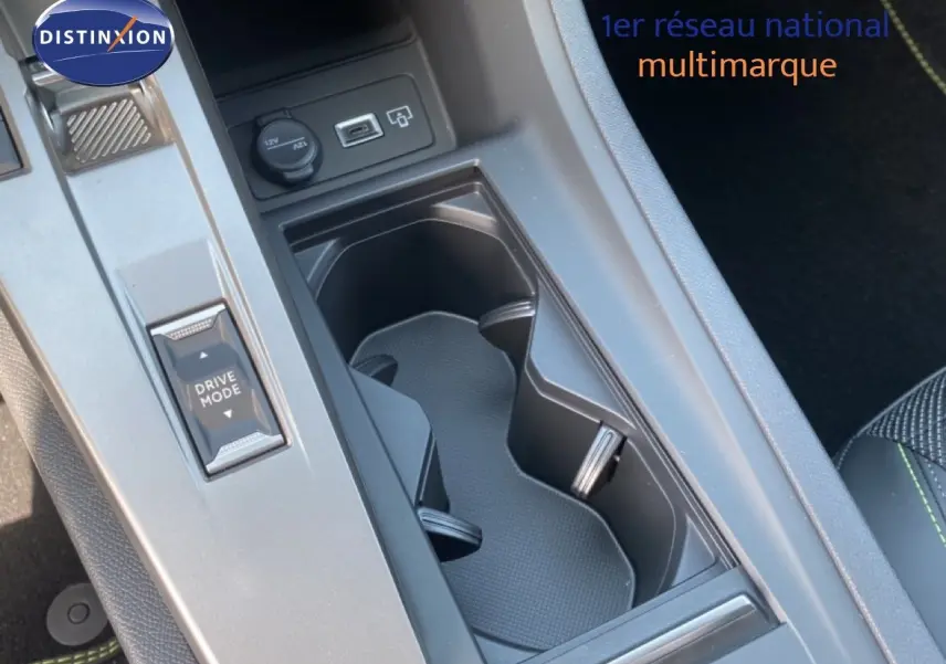 Vue rapprochée de la console centrale noire avec porte-gobelets et bouton Drive Mode dans une Peugeot 308 Hybrid blanche.