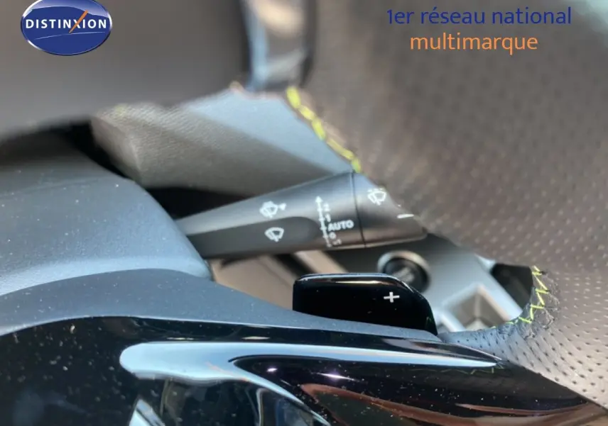 Gros plan sur la commande au volant et le levier de vitesse d'une Peugeot 308 Hybrid blanche, avec surpiqûres jaunes.