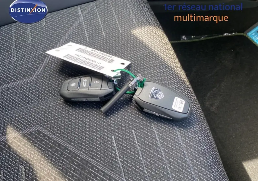 Gros plan sur les clés de la Peugeot 308 Hybrid 145ch GT posées sur un siège tissu gris foncé à motifs.