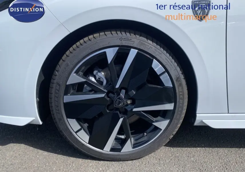 Gros plan sur la roue avant droite de la Peugeot 308 Hybrid blanche avec jante noire et argentée au design moderne.