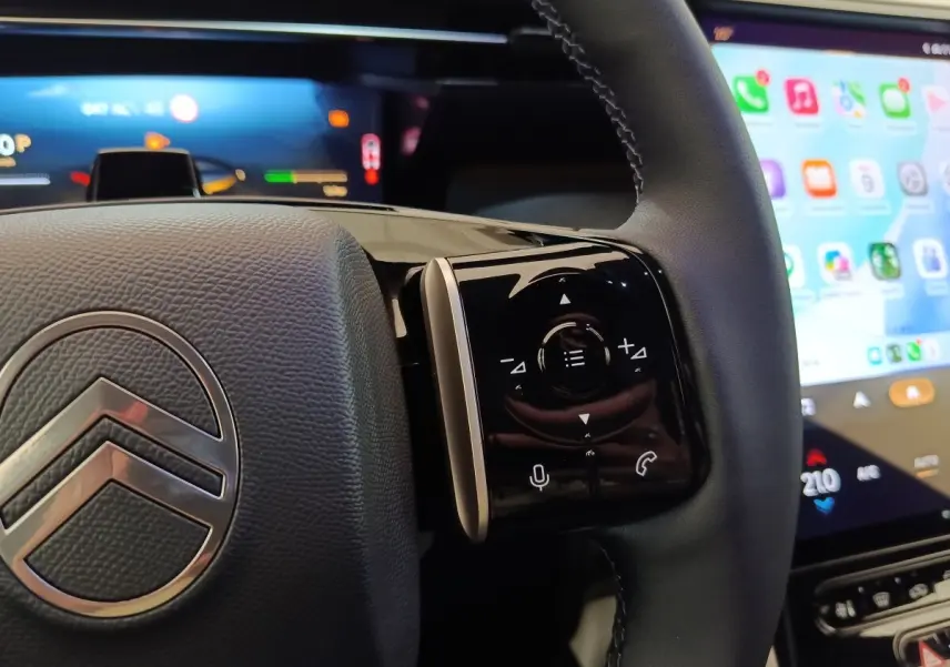 Gros plan sur le volant noir de la Citroën C5 hybride avec commandes multifonctions et écran tactile en arrière-plan.
