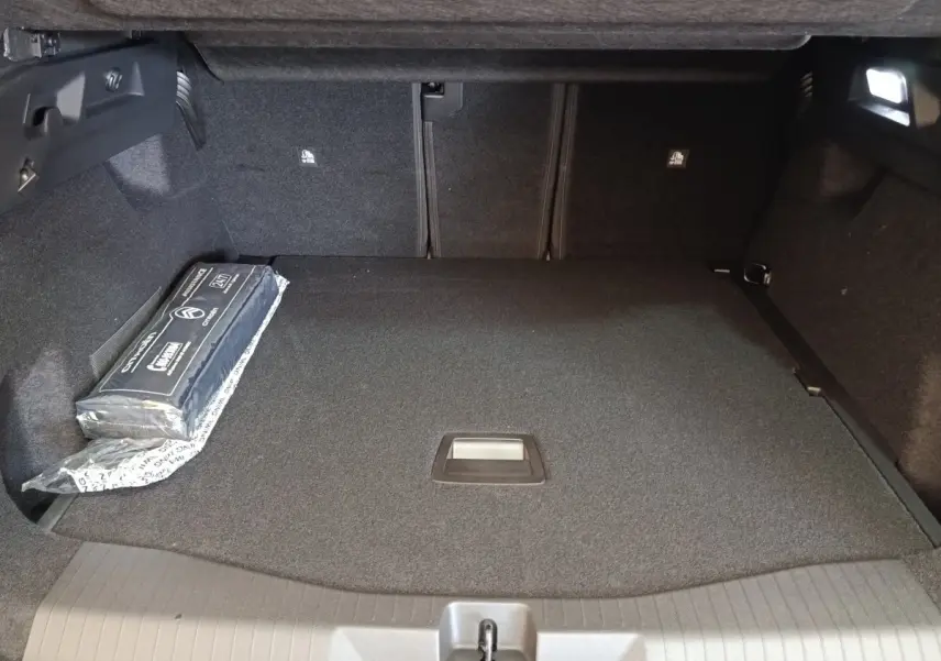 Coffre spacieux vu de face de la Citroën C5 Hybride 2026, avec tapis noir et kit de sécurité sur le côté gauche.