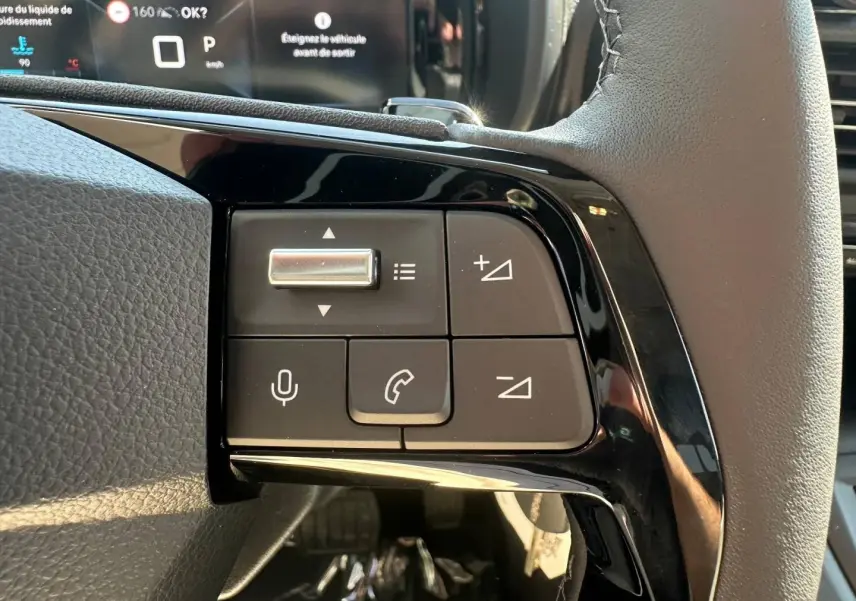 Gros plan sur les commandes au volant cuir noir du Citroën Berlingo 2026, version Sirkka Green, avec affichage numérique en arrière-plan.