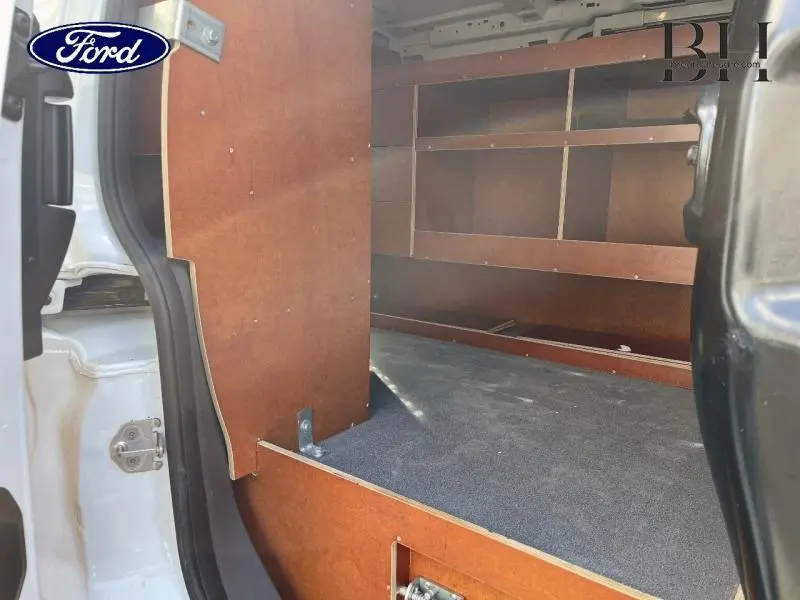 Vue intérieure depuis la porte latérale gauche du Ford Transit Connect blanc glacier, montrant l'aménagement bois de l'espace de chargement.