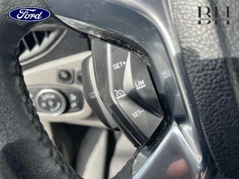 Gros plan sur les commandes de régulateur de vitesse au volant noir du Ford Transit Connect blanc glacier, intérieur avant gauche.