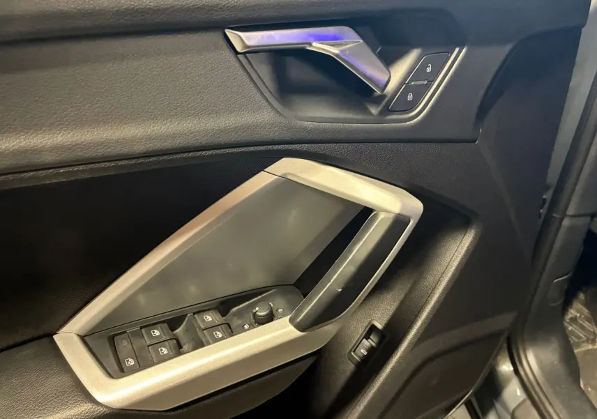 Vue rapprochée de la porte avant gauche de l'Audi Q3 Sportback gris, avec commandes de vitres et verrouillage.