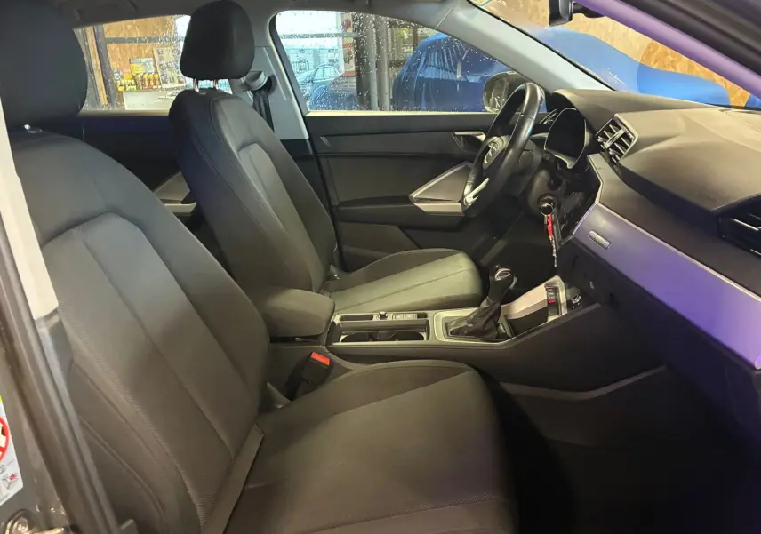 Vue intérieure côté conducteur de l'Audi Q3 Sportback gris, montrant les sièges avant noirs et la console centrale moderne.