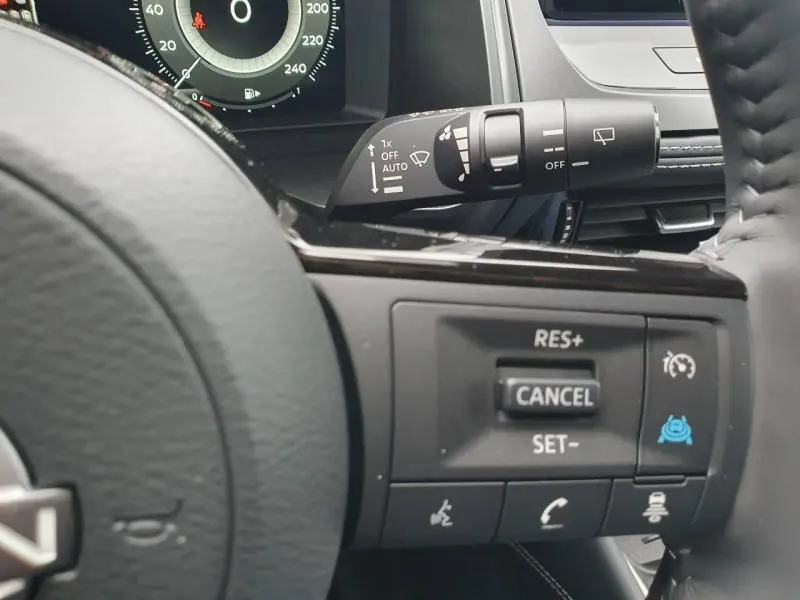 Gros plan sur commandes au volant et levier d'essuie-glace du Nissan Qashqai Hybrid e-POWER gris, tableau de bord partiellement visible.