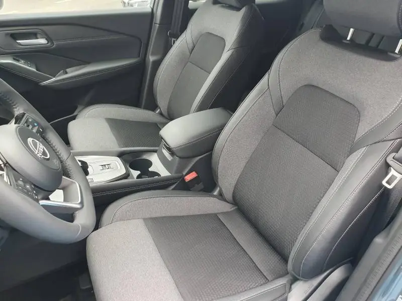 Vue intérieure rapprochée des sièges avant gris mixte tissu du Nissan Qashqai Hybrid e-POWER 2026 avec accoudoir central et volant multifonction.