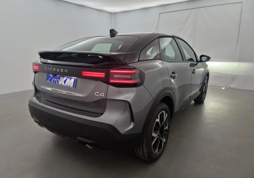 Vue 3/4 arrière droite d'une Citroën C4 2025 gris Mercury/noir avec feux arrière allumés dans un studio blanc.