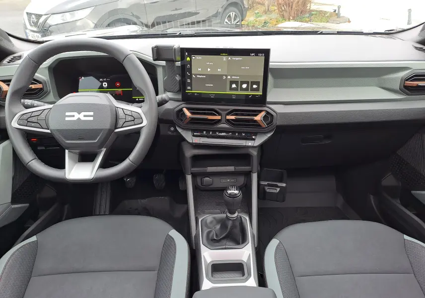 Vue intérieure avant du tableau de bord du Dacia Bigster 2025 avec volant multifonction, écran tactile et levier de vitesse manuel.