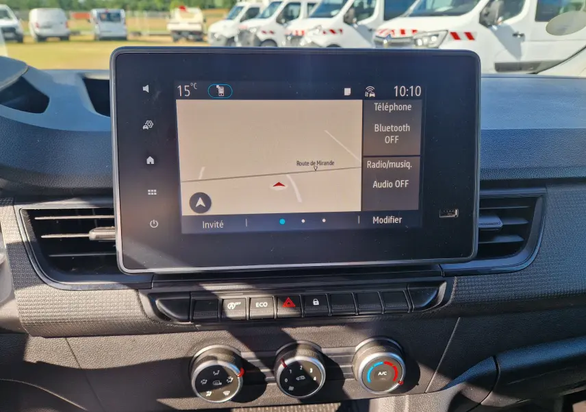 Vue rapprochée de l’écran tactile central et des commandes de climatisation du Renault Kangoo blanc 2023, intérieur fonctionnel.