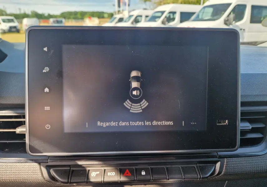Écran tactile central du Renault Kangoo 2023 blanc affichant l'alerte de détection d'obstacles avec vue intérieure.