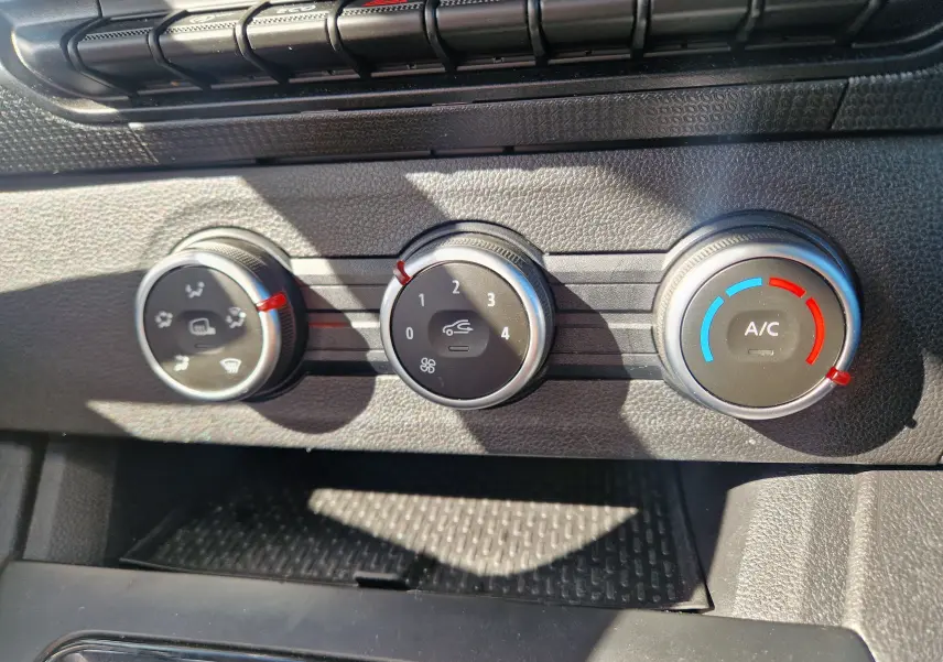 Gros plan sur les commandes de climatisation du Renault Kangoo blanc 2023, avec réglages manuels et boutons ronds.