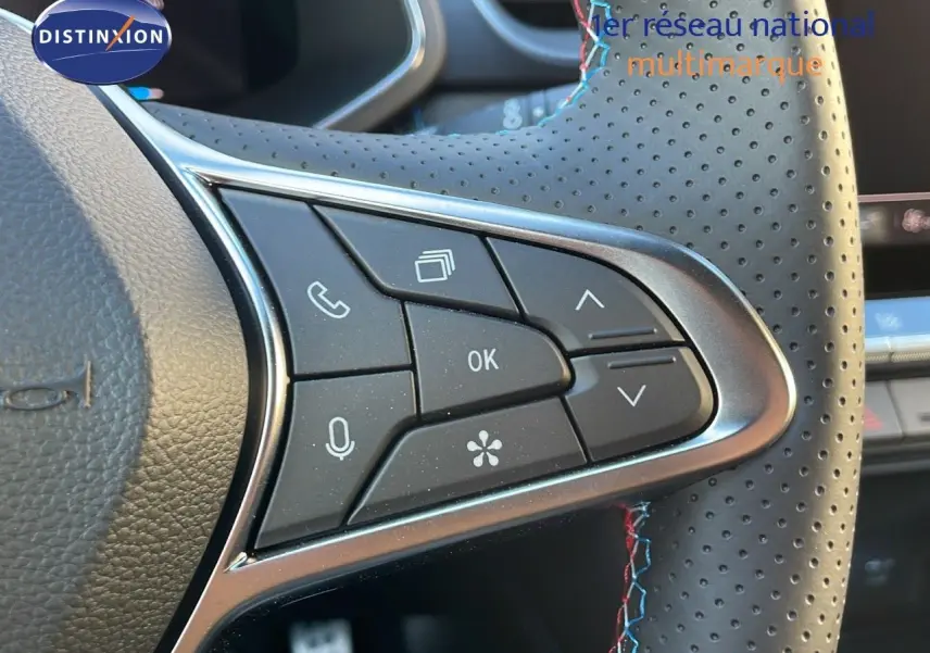 Gros plan sur les commandes multifonctions du volant en cuir noir perforé avec surpiqûres bleues et rouges du Renault Captur E-Tech.