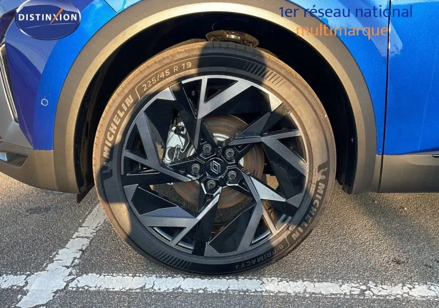 Gros plan sur la roue avant gauche du Renault Captur bleu Iron Metal avec jante noire au design géométrique.