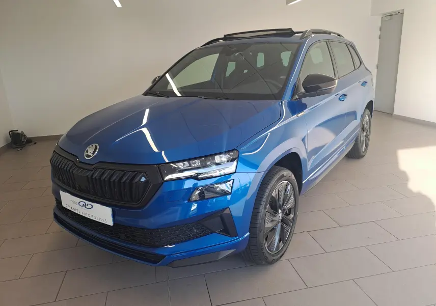Skoda Karoq Bleu RS en 3/4 avant droit, toit ouvrant panoramique et jantes sport visibles en intérieur showroom.