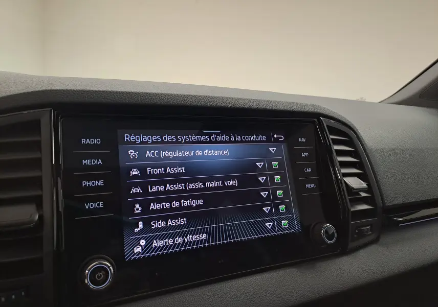 Écran tactile central du Skoda Karoq 2025 affichant les réglages des aides à la conduite dans un intérieur noir.