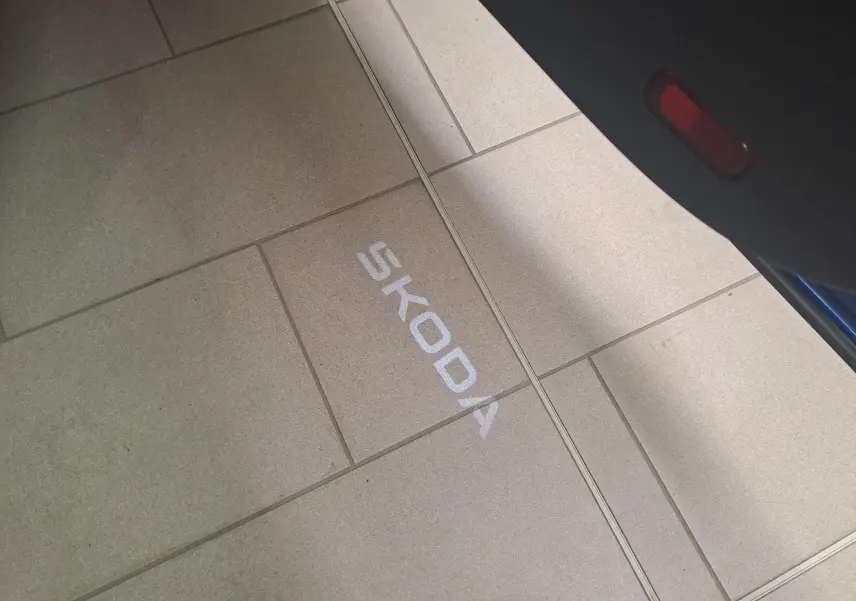 Projection lumineuse du logo SKODA au sol depuis la portière ouverte d'un SUV bleu RS.