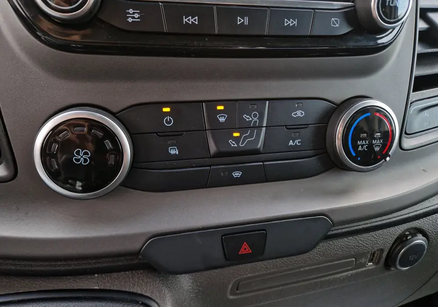 Gros plan sur la console centrale du Ford Transit Custom blanc, montrant les commandes de climatisation et de ventilation.