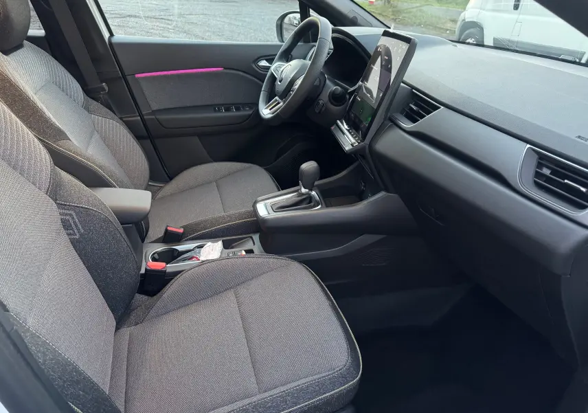 Vue intérieure côté conducteur du Renault Captur E-Tech Hybrid 2025, montrant sièges gris, volant et grand écran tactile vertical.