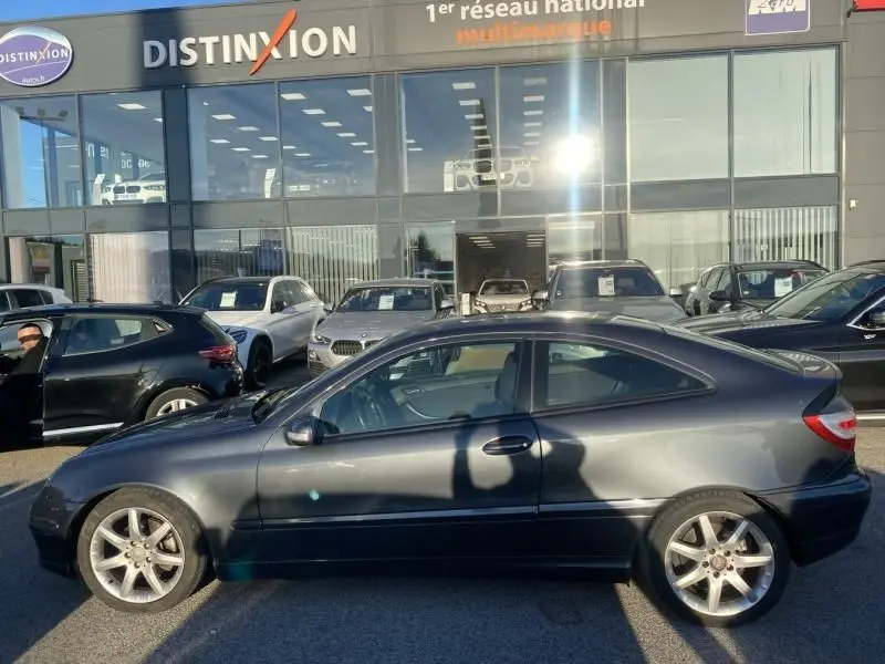 Profil côté gauche d'une Mercedes Classe C Coupé Sport 220 CDI gris foncé métal de 2008, garée devant un concessionnaire.