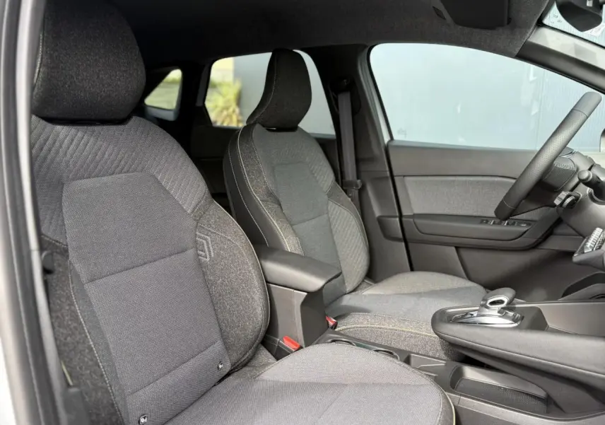 Vue intérieure côté conducteur du Renault Symbioz gris Rafale, mettant en valeur les sièges en tissu et la console centrale avec levier de vitesses automatique.