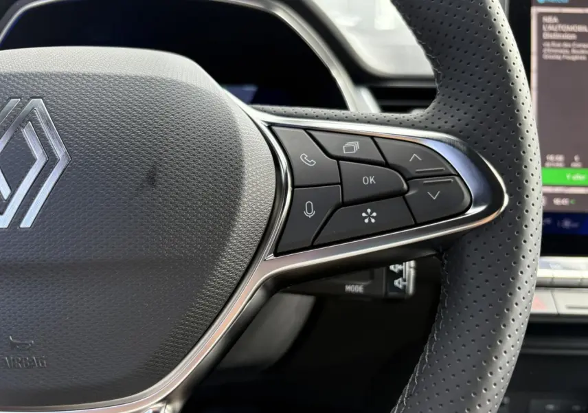Gros plan sur le volant en cuir perforé de la Renault SYMBIOZ gris Rafale, avec commandes multifonctions et écran tactile en arrière-plan.