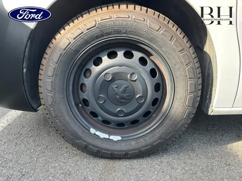 Gros plan sur la roue avant gauche noire du Peugeot Expert Fourgon blanc Banquise, avec logo Peugeot au centre.