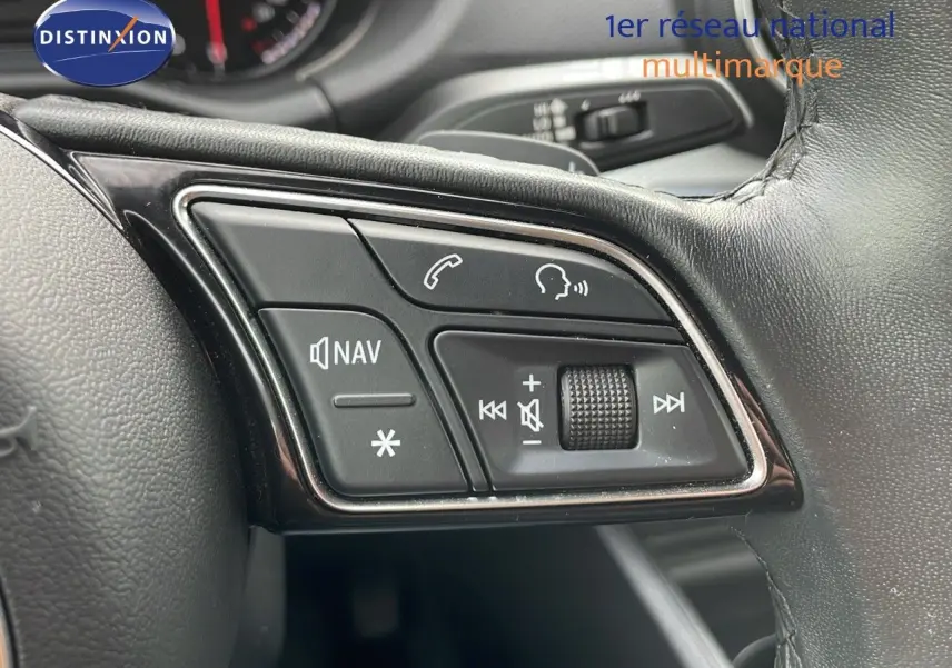 Gros plan sur les commandes du volant d’un Audi Q2 noir mito metal, mettant en valeur les boutons de navigation et audio.
