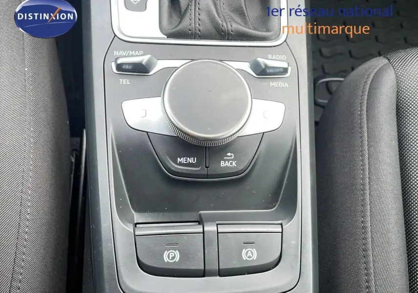 Vue rapprochée de la console centrale noire de l'Audi Q2 35 TFSI 2023, avec commandes multimédia et frein électronique.