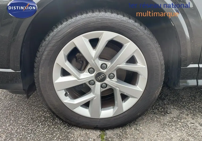 Gros plan sur la roue avant gauche d’un Audi Q2 noir mito metal, mettant en valeur la jante argentée à cinq branches.