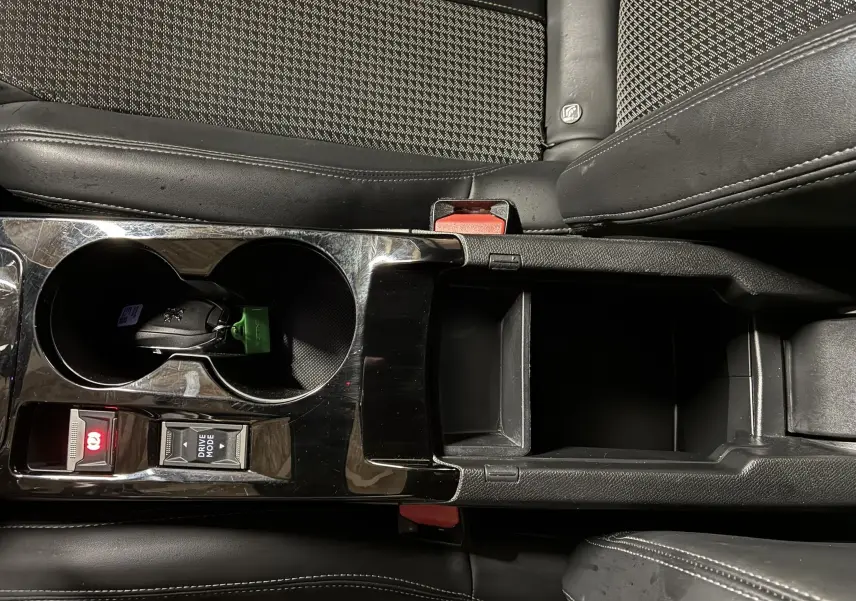 Vue rapprochée de la console centrale noire du Peugeot 2008 1.5 BlueHDi 130 GT Line avec porte-gobelets et rangement ouvert.