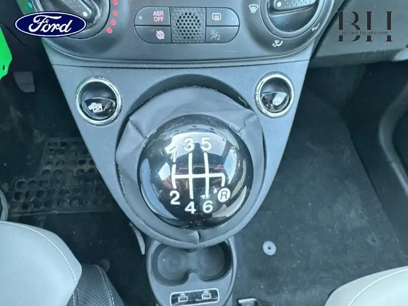 Gros plan sur le levier de vitesses manuel noir de la FIAT 500 blanche, entouré de commandes et porte-gobelets.