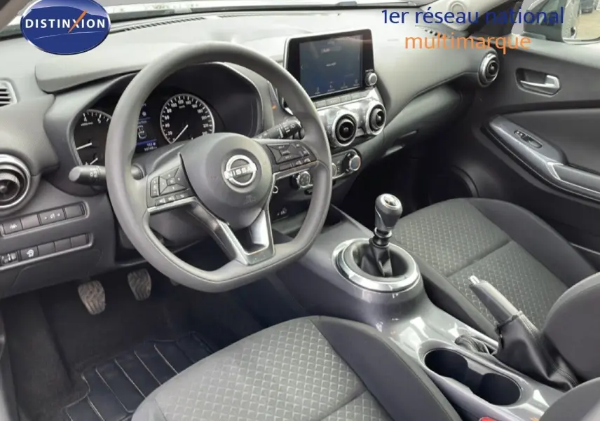 Vue intérieure de face côté conducteur du Nissan Juke 2023, volant multifonction et levier de vitesse manuel, finition tissu gris-noir.