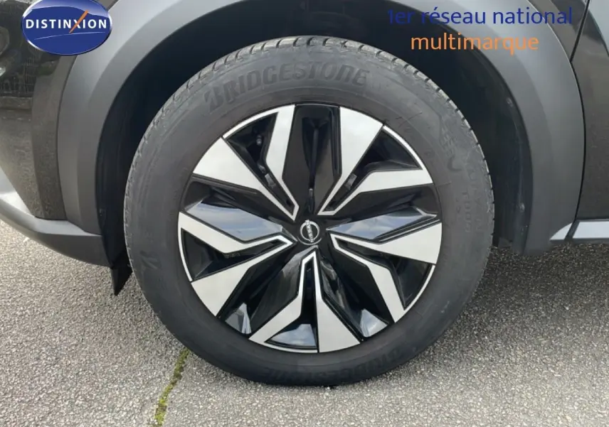 Gros plan sur la roue avant droite d’un Nissan Juke noir perle métal 2023 avec jante noire et argentée.