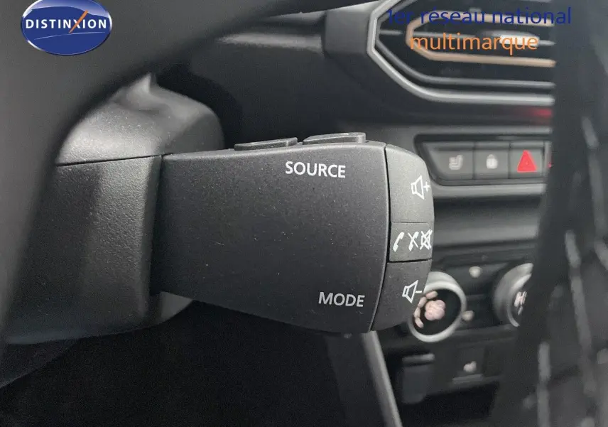 Gros plan sur la commande au volant du Dacia Jogger 2026, avec boutons source et mode, intérieur noir visible en arrière-plan.