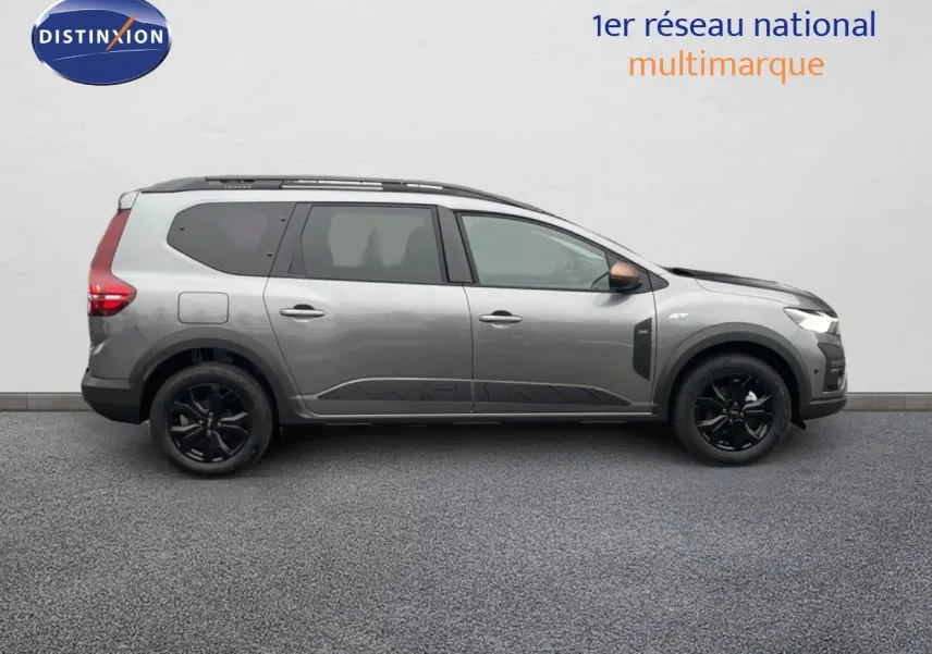 Vue de profil côté gauche d'un Dacia Jogger gris schiste métal avec jantes noires et toit équipé de barres de toit.