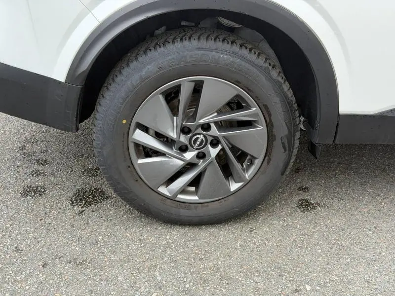 Gros plan sur la roue avant droite d’un Nissan Qashqai blanc nacré avec jante alu gris foncé au design moderne.