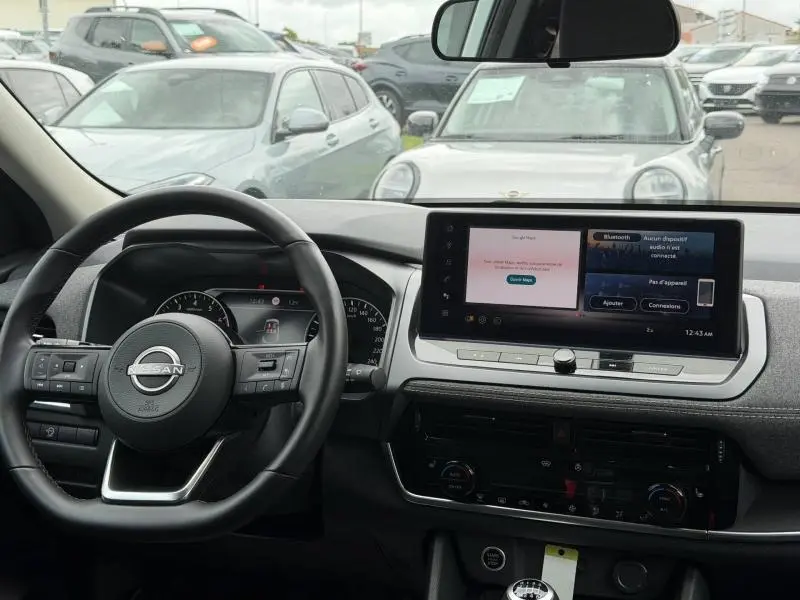 Vue intérieure du tableau de bord du Nissan Qashqai blanc nacré 2025, avec écran tactile et volant multifonction cuir.