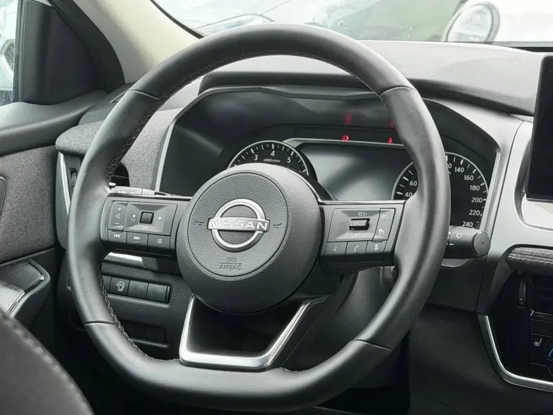 Vue rapprochée du volant cuir noir multifonction du Nissan Qashqai 2025 avec tableau de bord digital en arrière-plan.