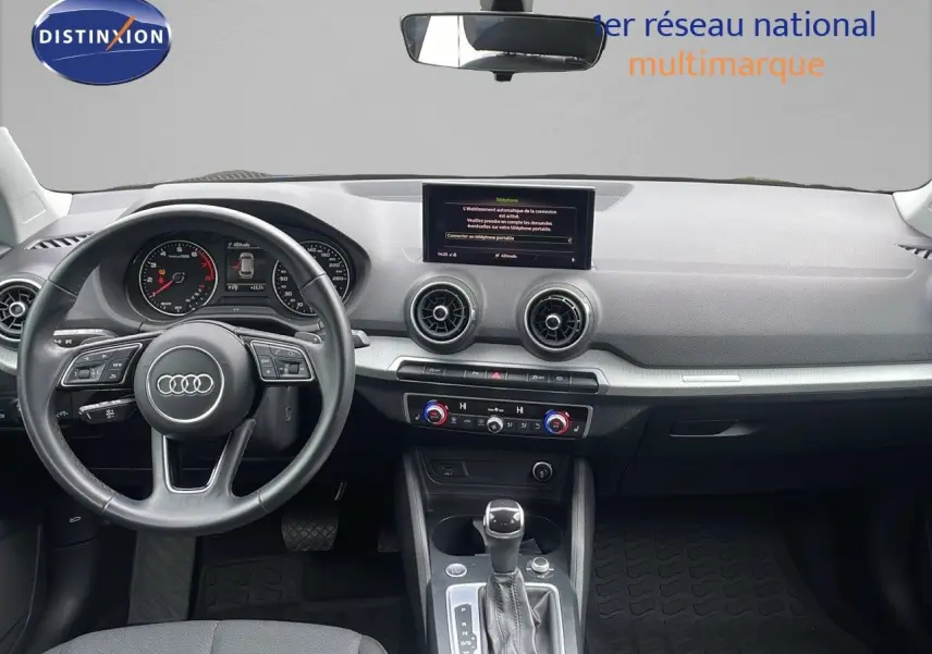 Vue intérieure avant de l'Audi Q2 35 TFSI S-Line 2023, tableau de bord gris avec volant multifonction et écran central.