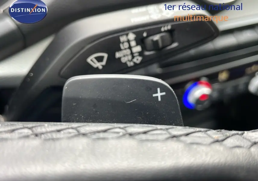 Gros plan sur la palette de passage de vitesses droite du volant d'un Audi Q2 noir mito metal, avec commandes de climatisation en arrière-plan.