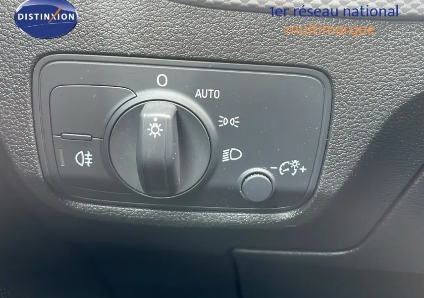 Gros plan sur le bouton de commande des phares de l'Audi Q2 noir mito metal, avec réglage automatique et options éclairage.