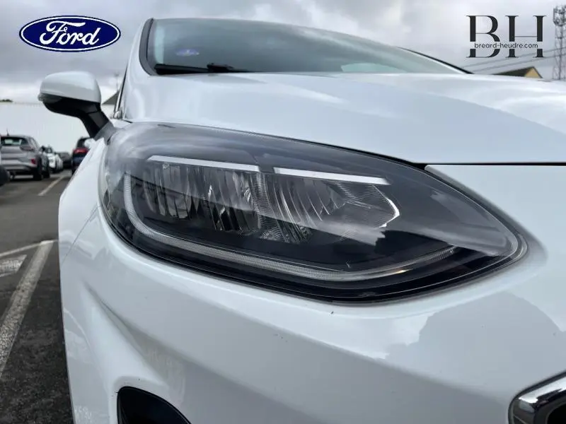 Gros plan sur le phare avant droit de la Ford Fiesta blanc glacier 2022 avec calandre chromée et rétroviseur blanc.