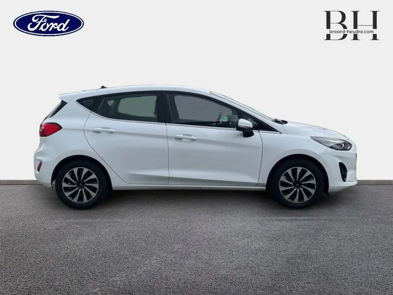 Vue de profil côté gauche d'une Ford Fiesta Titanium Business blanche Glacier avec jantes alu et becquet arrière.