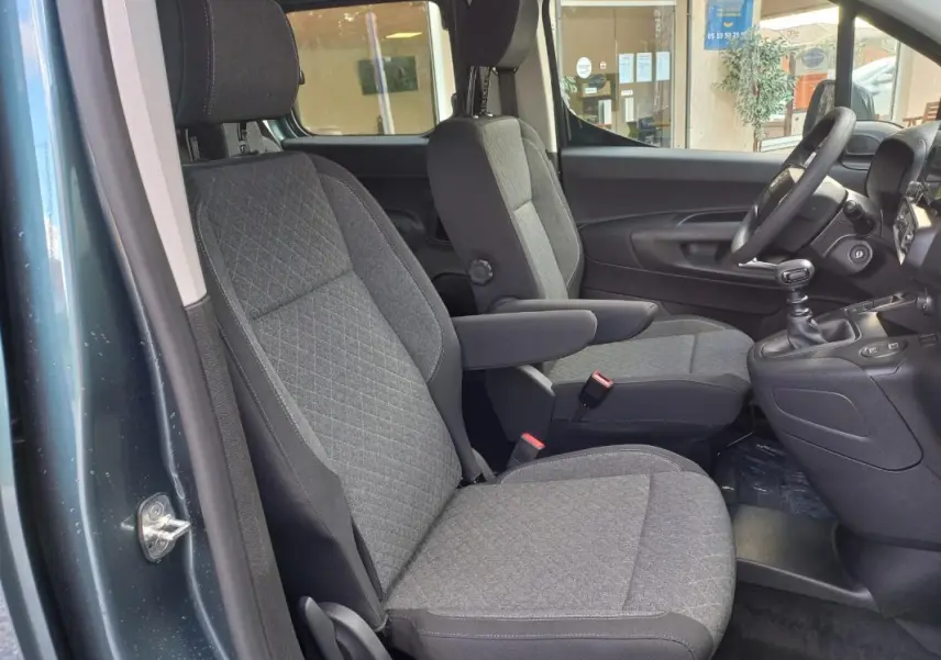 Vue intérieure côté conducteur de l'Opel Combo Life M 2025 bleu, montrant les sièges avant en tissu gris et la boîte manuelle.