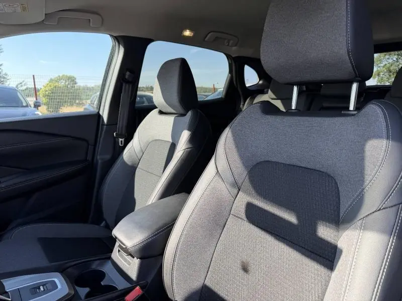 Vue intérieure côté avant droit du Nissan Qashqai 2025, sièges tissu noir avec accoudoir central et console.
